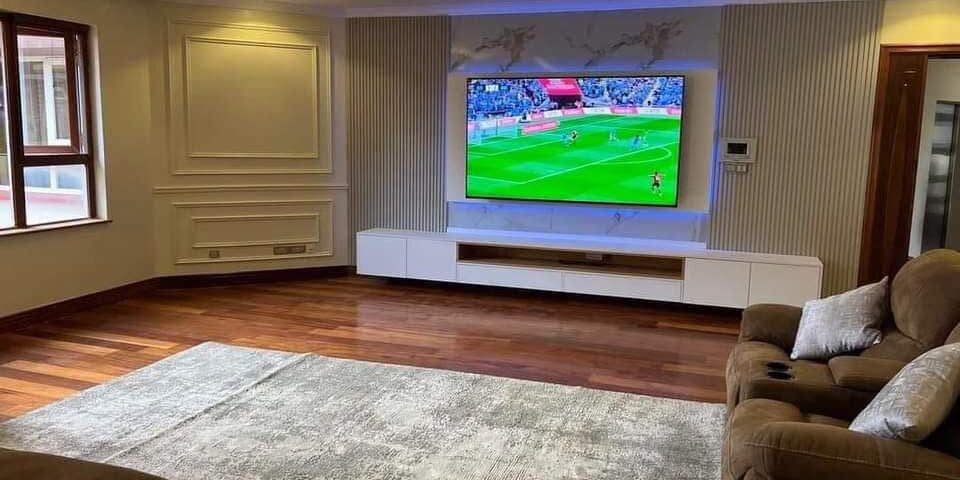 Living room interior with wooden flooring, wall panelling and custom TV unit by Shivin Interiors